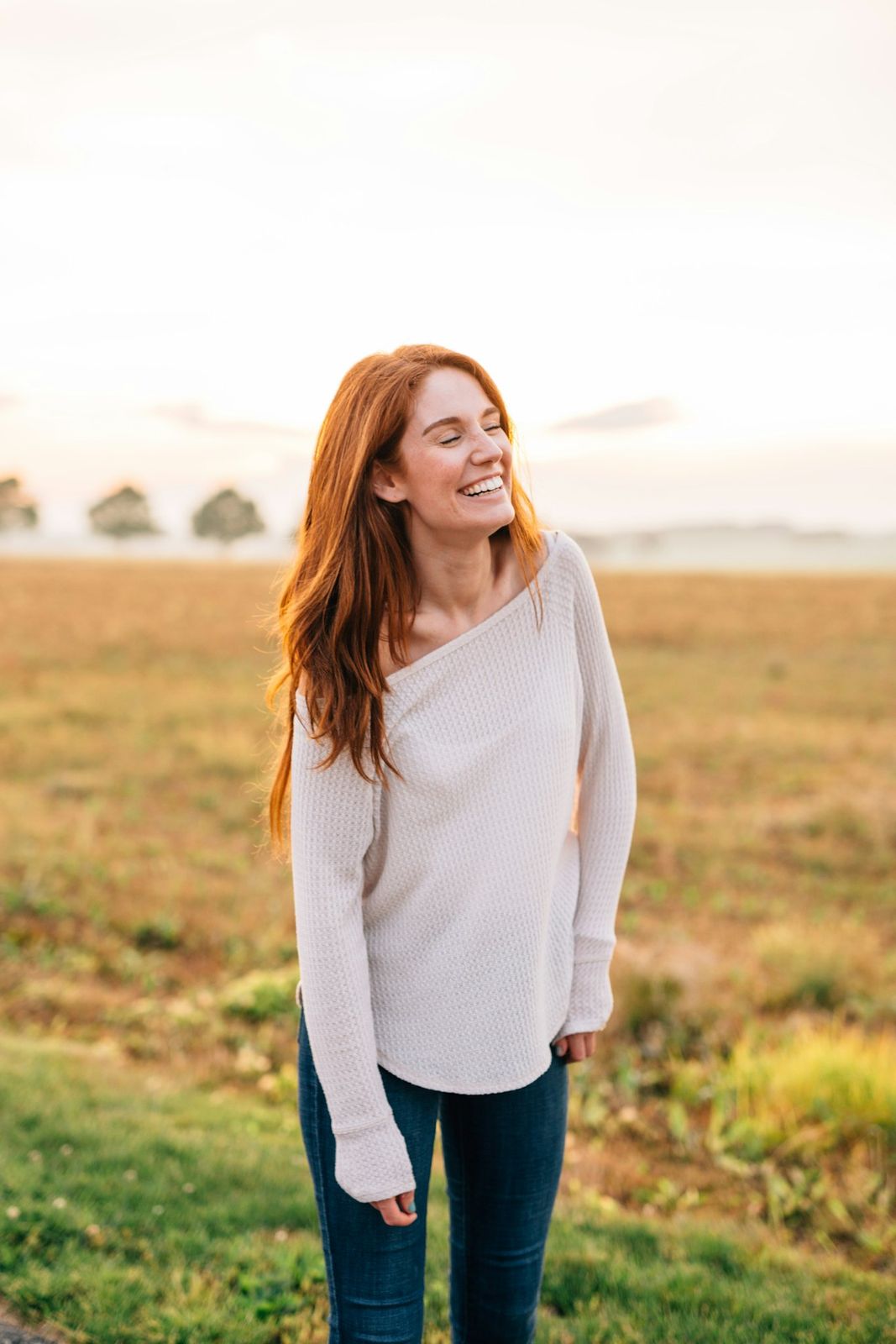 Een vrouw in een witte top lacht in een veld